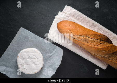 Brie Käse und Baguette auf einem dunklen Tisch Stockfoto