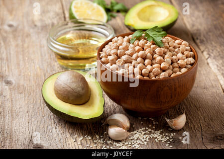 Zutaten für das Kochen mit Avocado Hummus: Kichererbsen, Avocados, Olivenöl, Sesamöl, Knoblauch, Kalk auf den alten hölzernen Hintergrund Stockfoto