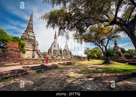 Tourist-Frau im roten Kostüm zu Fuß in der Nähe von alten verfallenen Stupa in Ayutthaya Historical Park, Thailand Stockfoto