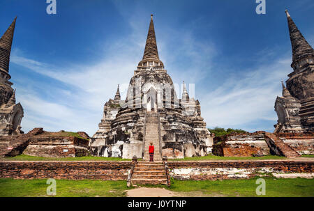 Tourist-Frau im roten Kostüm zu Fuß in der Nähe von alten verfallenen Stupa in Ayutthaya Historical Park, Thailand Stockfoto