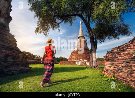 Tourist-Frau im roten Kostüm, Wandern in der Nähe von alten verfallenen Stupa mit Fotokamera in Ayutthaya Historical Park, Thailand Stockfoto