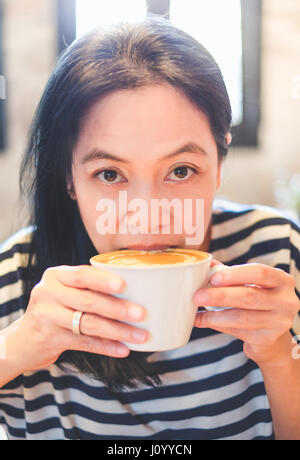 Nahaufnahme Gesicht Asiatin Schluck heißen Cappuccino Kaffee im Café Shop, heißes Getränk zu trinken. Stockfoto