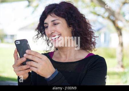 Closeup Porträt, junge happy Business Woman in Black Shirt stehen, ihr cellphone Checking, isoliert im Freien Hintergrund. Business Communication Stockfoto