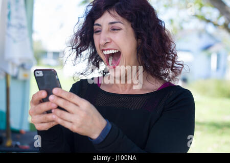 Closeup Porträt, junge happy Business Woman in Black Shirt stehen, ihr cellphone Checking, isoliert im Freien Hintergrund. Business Communication Stockfoto