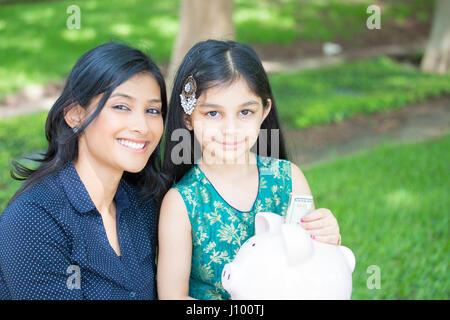 Closeup Portrait, Familie halten Piggy Einsparungen, bereit für Einsparungen, isoliert grüne Bäume Rasen Background. Geld-Aufbau-Strategie Stockfoto