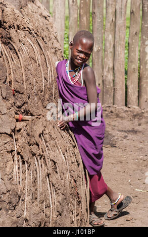 Maasai Mädchen in lila außerhalb ihrer Hütte. Stockfoto