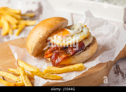 Hamburger mit Spiegelei, Speck und Pommes Frites. Stockfoto