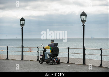 Worthing, West Sussex, UK. Ein Mann sitzt auf einem Mobility Scooter blickt zum Meer vom Ende des Worthing Pier während einer bedeckt und bewölkten Tag. Stockfoto