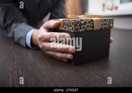 Hände des Mannes halten eine Box in einem Business-Anzug eingepackt durch einen Bogen Stockfoto