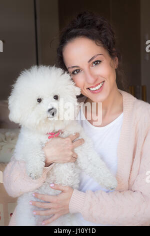 Porträt einer jungen Frau mit ihrem Hund Bichon Frise an ihrem Haus. Stockfoto