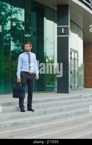 Porträt von gut aussehenden jungen Mann stehend auf Schritte außerhalb modernes Bürogebäude mit Glasfronten Stockfoto