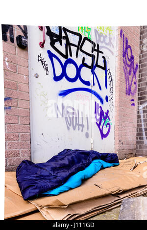 Einen Schlafsack und Kartons auf dem Boden in einer Gasse hinter einem Bürogebäude, verwendet durch einen Obdachlosen um zu schlafen. Stockfoto