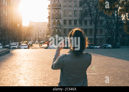 Frau fotografieren auf einem Smartphone in einer alten Stadt bei Sonnenuntergang, Blick von der Rückseite Stockfoto