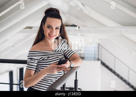 Lächelnde Geschäftsfrau mit ihrem Handy im Internet surfen und beim Blick in die Kamera Lächeln. Stockfoto