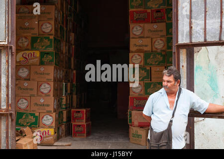 Ein Mann stand vor Gebäude für die Lagerung von Fällen von Bier in Havanna, Kuba. Stockfoto