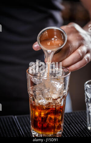 Barkeeper gießt Alkohol aus einem Messgerät Glas in ein Glas mit Eis Stockfoto