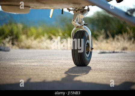 Eine hintere Fahrwerk und Unterlegkeile eines kleinen Flugzeugs auf dem Boden mit verschwommenen Natur und Verkehr Kegel im Hintergrund. Stockfoto