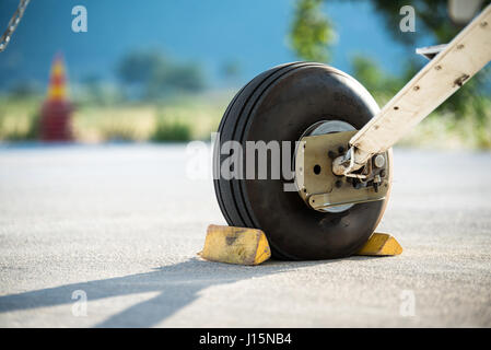 Eine hintere Fahrwerk und Unterlegkeile eines kleinen Flugzeugs auf dem Boden mit verschwommenen Natur und Verkehr Kegel im Hintergrund. Stockfoto