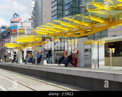 Exchange Square im Zentrum von Manchester, England, zeigt Menschen auf der Straßenbahn-Plattform, mit der bunten farbenfrohen Printworks im Hintergrund. Stockfoto