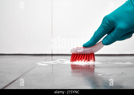 Männliche Hand mit roten Bürstenreinigung die Fliesen im Bad auf der Etage. Stockfoto