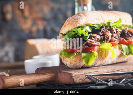 Beef Sandwich mit Tomaten und Salat auf Holzbrett mit Zutaten. Stockfoto