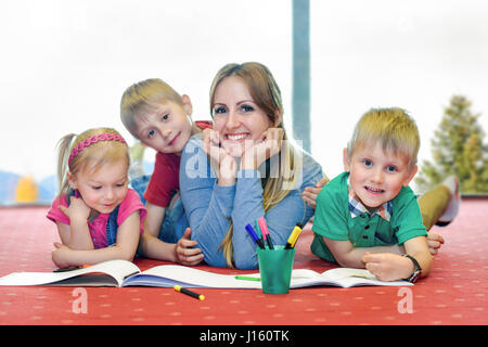 Glückliche Mutter mit ihren Kindern auf dem Teppich in der Wohnung liegt und spielt mit der Färbung der Bilder Stockfoto