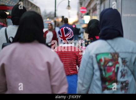 Eine Gesamtansicht eines kleinen Jungen mit einem Union Jack Hut begleitet von Muslimin in der Oxford Street, London. Stockfoto