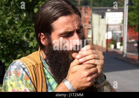 Mann mit langen Haaren und Bart, Rauchen auf der Straße Stockfoto