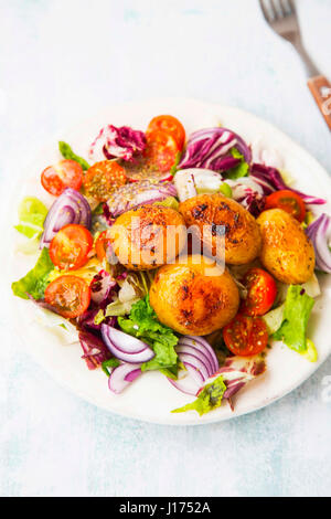 Neue Kartoffeln in einem Teller mit Gemüse-Salat mit Zwiebeln, grünem Salat, Tomaten gewürzt Stockfoto
