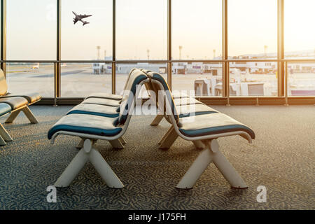 Leere Stühle in der Abflughalle am Flughafen mit Flugzeug abheben bei Sonnenuntergang. Reise und Transport in Flughafen-Konzepte. Stockfoto