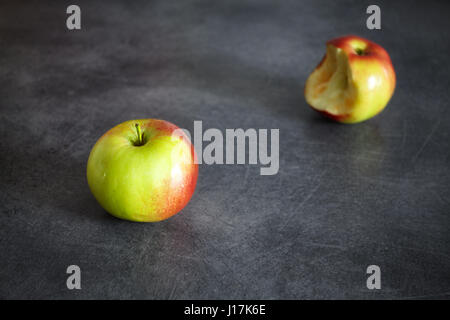 Zwei reife Äpfel, ein ganzes und eine gebissen auf einem dunklen Hintergrund, Tiefenschärfe, Platz für Text. Stockfoto