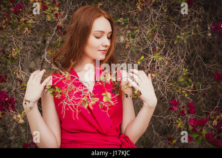 Schöne rothaarige Mädchen im roten Kleid im Busch. Stockfoto