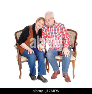 Ein älteres Ehepaar in Senioren sitzen auf zwei Stühlen, die Frau mit dem Kopf auf die Schulter des Mannes, für weißen Hintergrund isoliert. Stockfoto