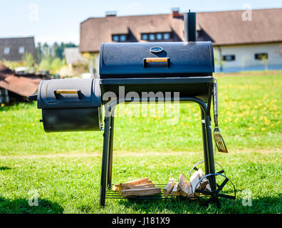 Zubereitung von köstlichen Fleisch in langsamen Kochen Raucher im Hinterhof. Einfach zu bedienen zylindrische Raucher bei Familie Hinterhof Barbecue - Grill Picknick. Stockfoto