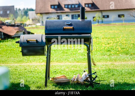 Zubereitung von köstlichen Fleisch in langsamen Kochen Raucher im Hinterhof. Einfach zu bedienen zylindrische Raucher bei Familie Hinterhof Barbecue - Grill Picknick. Stockfoto