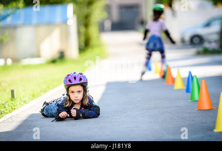 Kind fiel beim Lernen auf Rollschuh auf der Straße. Zwillingsmädchen üben sicher Inline Skates unterwegs ein Haus Einfahrt tragen von Schutzkleidung - Stockfoto