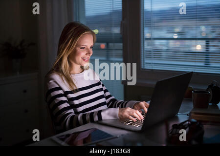 Frau am Schreibtisch sitzen und arbeiten am Laptop in der Nacht. Stockfoto