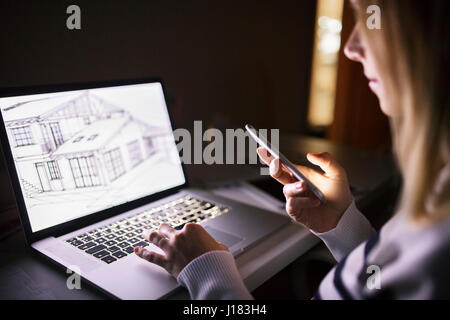 Frau an der Rezeption, mit Smartphone, nachts am Laptop arbeiten. Stockfoto