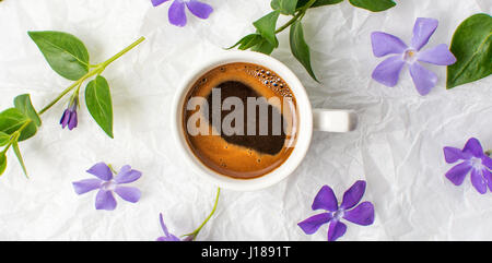 Tasse Kaffee und lila Frühlingsblumen auf Bettwäsche Stockfoto