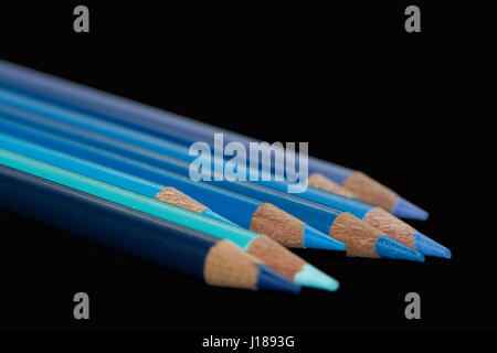 Acht blauen Farbstifte verschiedener Farbtöne und Schattierungen aufgereiht mit gestaffelten Längen mit einem dunklen schwarzen Hintergrund. Stockfoto
