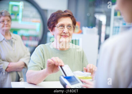 Ältere Frau bezahlen mit Kreditkarte in Apotheke Stockfoto