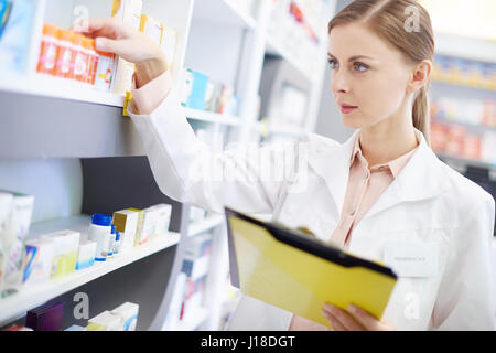 Junger Apotheker Blick auf Regal von Pillen Stockfoto