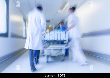 Eine Bewegung verschwommenes Foto eines Patienten auf Keilrahmen oder Gurney gedrängt mit Geschwindigkeit durch einen Krankenhausflur durch Ärzte & Krankenschwestern, Notfall Stockfoto