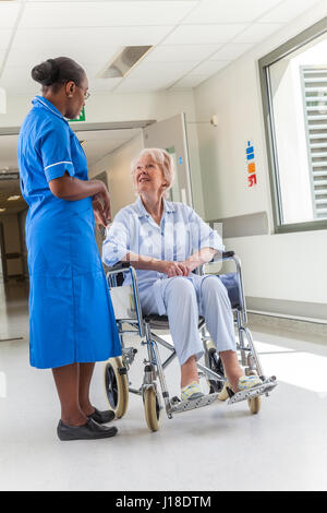 Ältere weibliche Frau Patienten im Rollstuhl sitzend im Krankenhausflur mit afroamerikanischen Krankenschwester Stockfoto