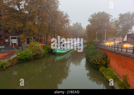 Nebel hüllt lange Boote vertäut am Canal du Midi und die umliegenden Gebäude in Toulouse im Süden Frankreichs. Stockfoto