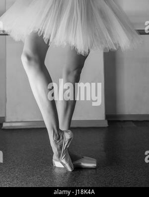 Eine Ballerina in Pointes und eine Packung erwärmt sich vor die Tanzstunde. Lange schlanke weibliche Füße. Klassisches Ballett. Primaballerina. Schwarz / weiß Foto Stockfoto