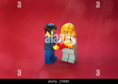 LEGO Eltern ihr neue Baby in ihren Armen hält. Stehend auf einem roten Hintergrund Stockfoto