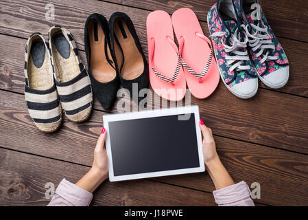 Weibliche schuhe Sammlung auf Holztisch mit Frau Hände halten Weiße digitale Tablet Stockfoto