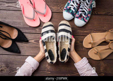 Weibliche schuhe Sammlung auf Holztisch mit Woman's Hände, die ein Paar Schuhe Stockfoto