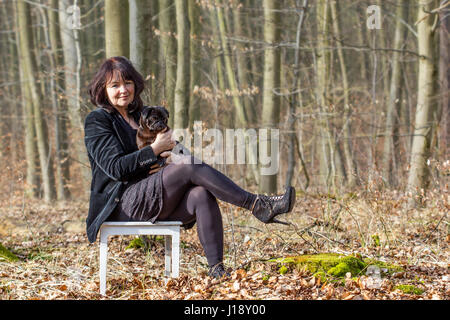 Eine Frau in schwarzer Kleidung mit einem süßen, schwarzen Mops auf einen weißen Stuhl Stockfoto